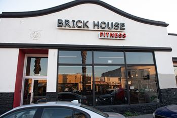 A white building with a red door and a sign that says Brick House Fitness.